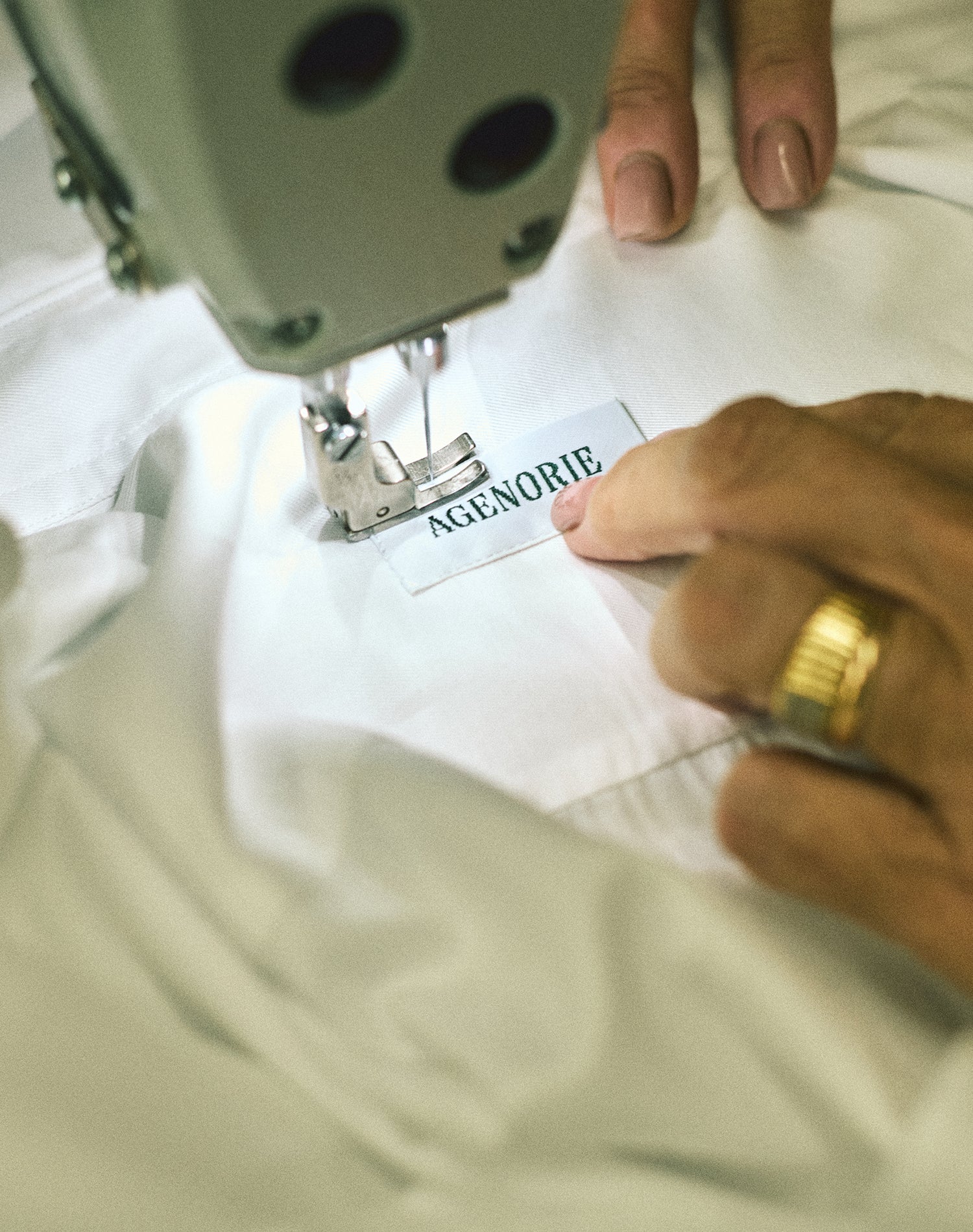 Cucitura a mano dell'etichetta Agenorie su una camicia bianca